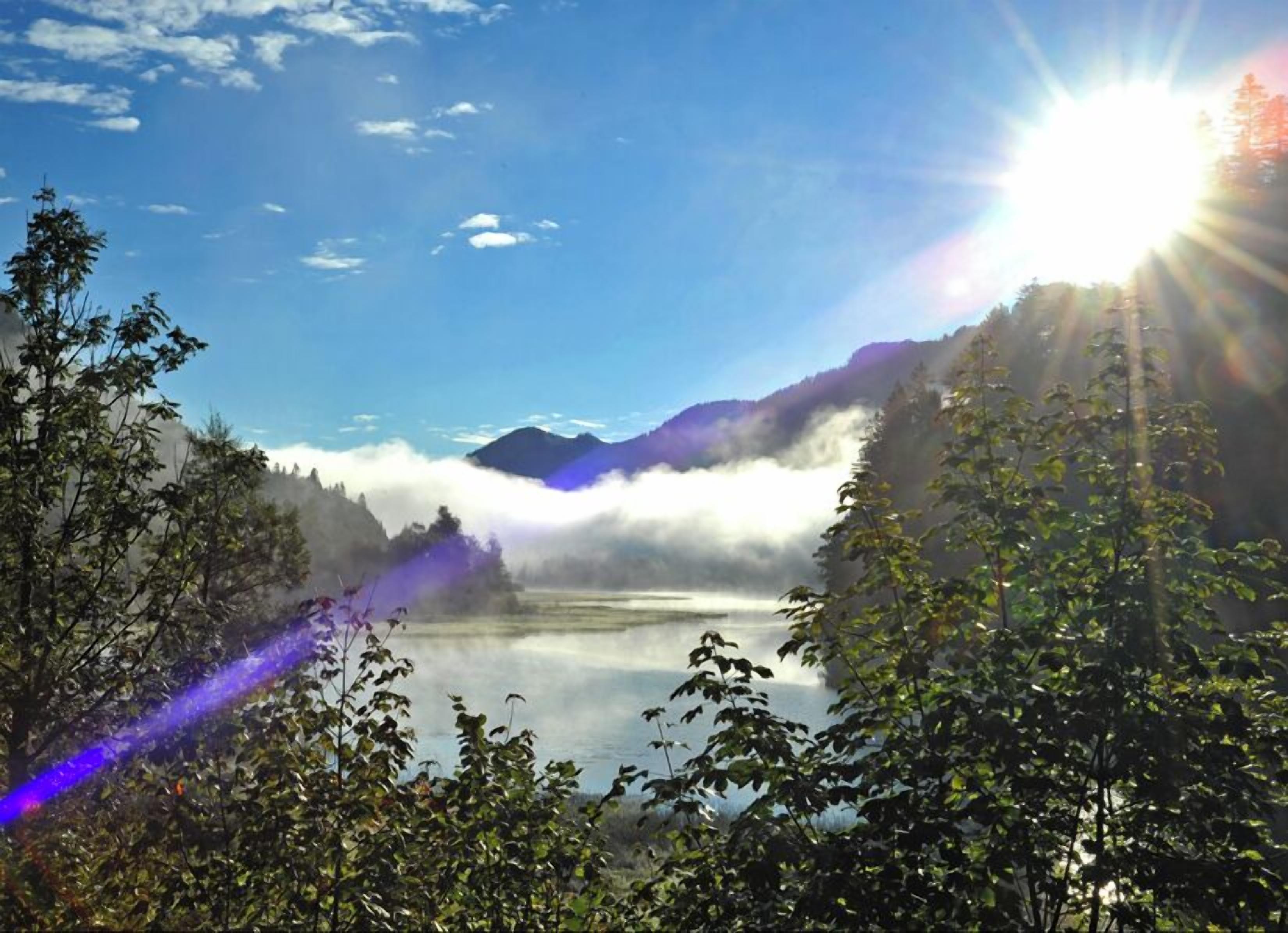 A serene lake surrounded by mountains and trees with sunlight shining through the foliage.