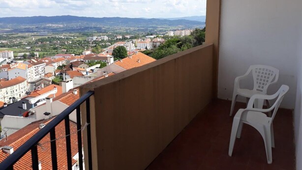 A balcony with a view of a town, a white plastic chair, and a tiled roof. - Apartment in the centre of Covilha (Covilha)