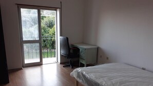 A room with a bed, a desk, and a chair. There is a sliding glass door leading to a balcony. - Apartment in the centre of Covilha (Covilha)