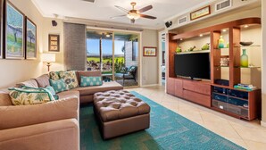 Una sala de estar con un sofá modular, un reposapiés, mueble de entretenimiento con televisor, y vistas a un patio a través de puertas de vidrio.