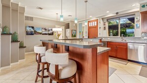 Una cocina moderna con una isla central, taburetes de bar, electrodomésticos de acero inoxidable y un amplio ventanal con vistas al verdor.