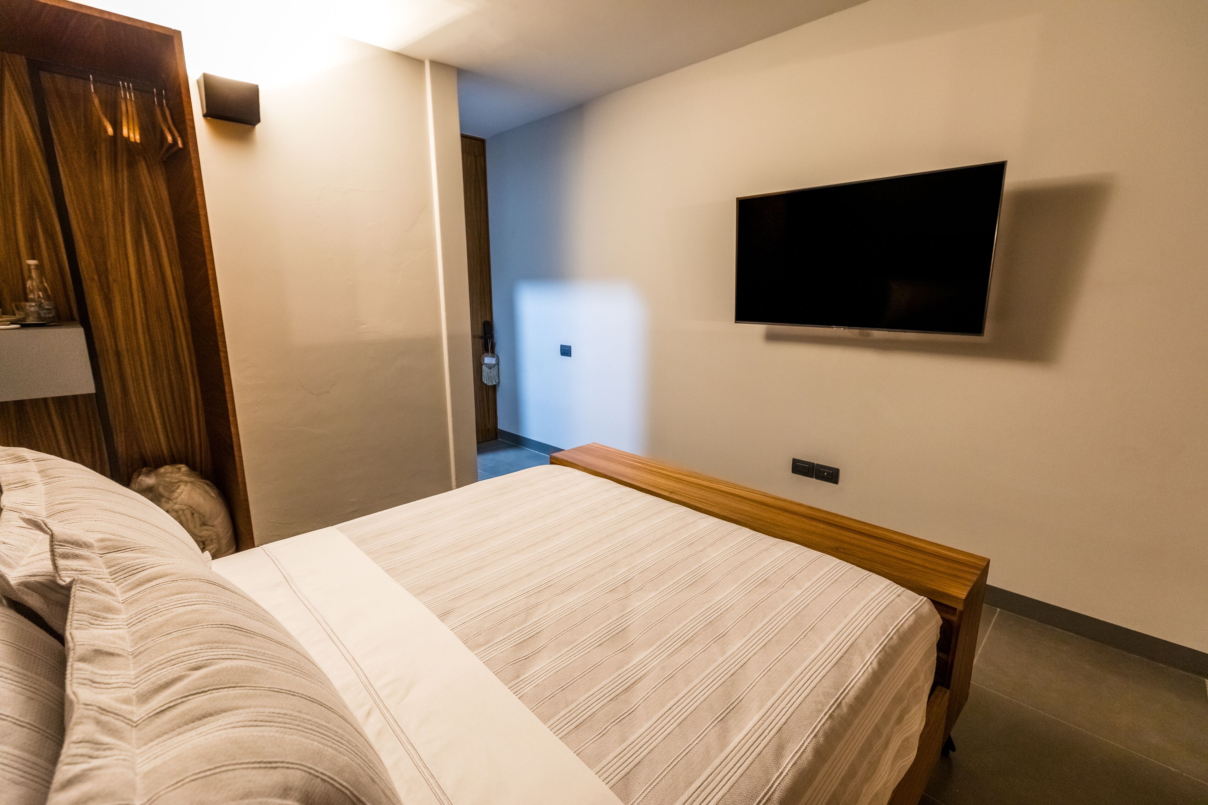 Una habitación de hotel con cama, televisión montada en la pared y una puerta que da a otra habitación.
