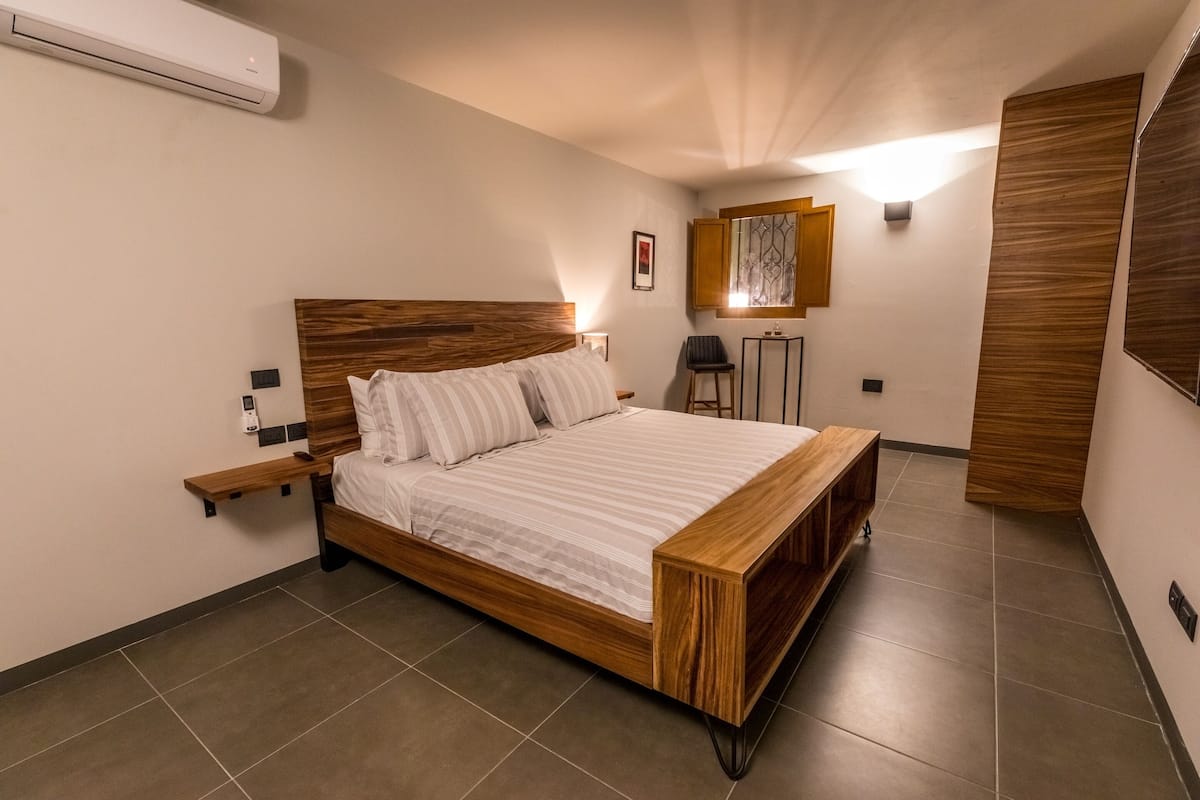 A modern bedroom with a wooden bed frame, a nightstand, and a wall-mounted air conditioner.