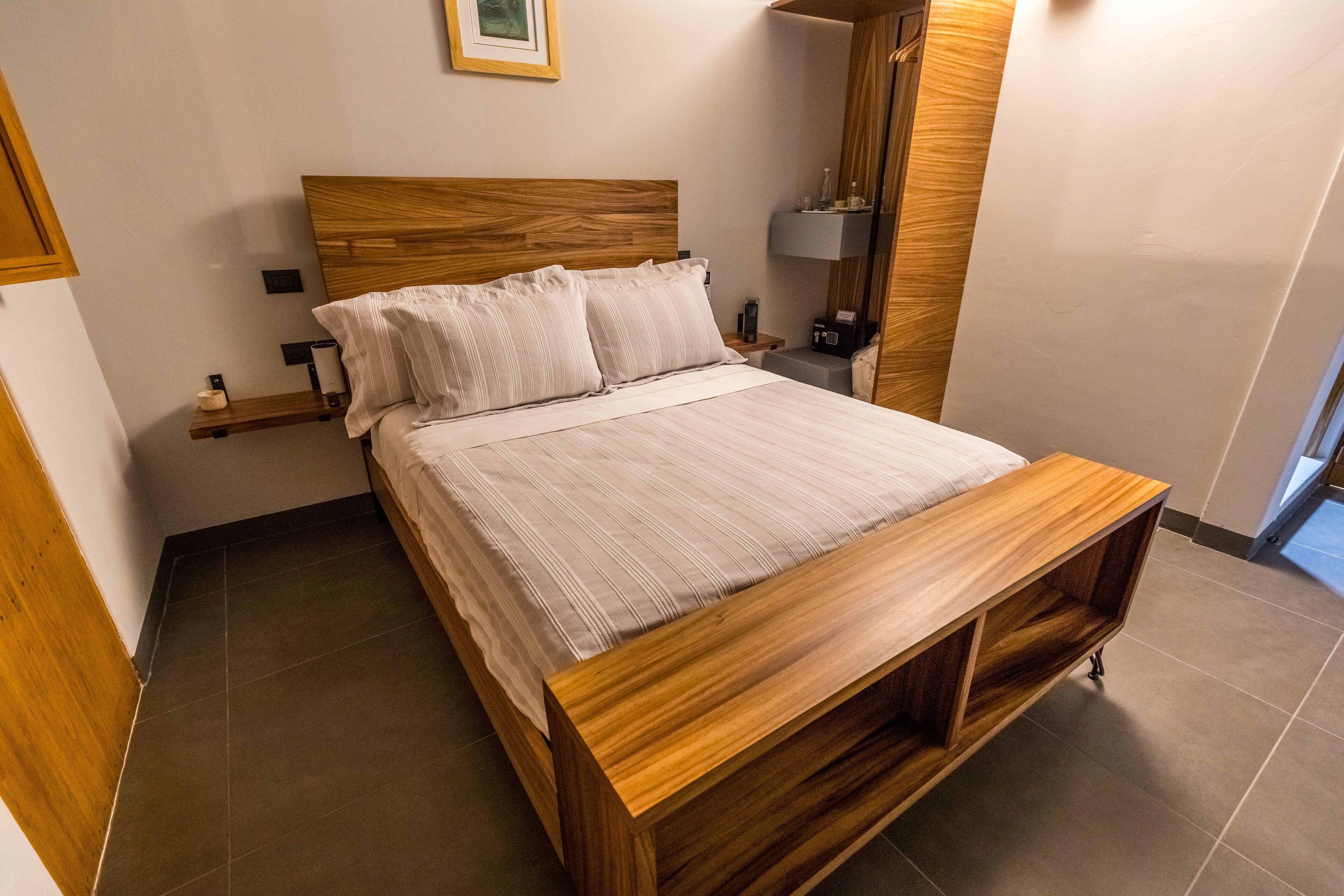 A modern bedroom with a wooden bed frame, a nightstand, a bedside table, and a wall-mounted lamp.