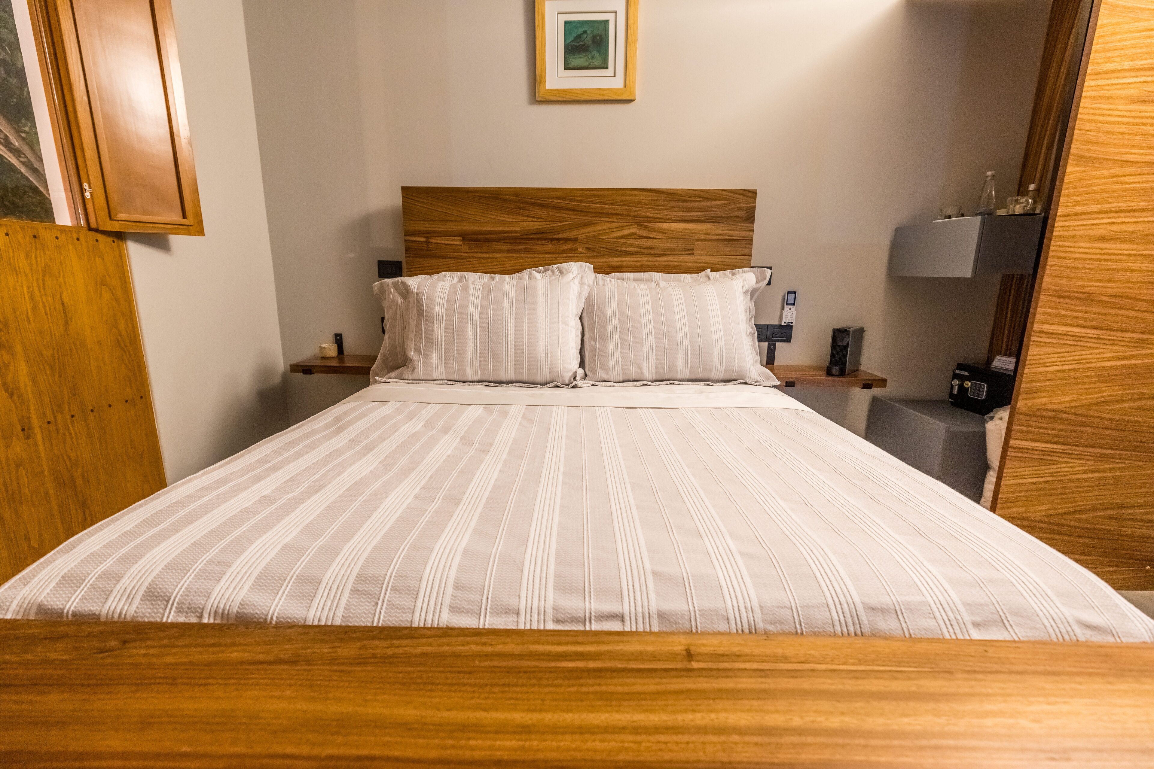 Un letto rifatto con cura, con copriletto a righe, una testiera in legno e due comodini con lampade e una sveglia.