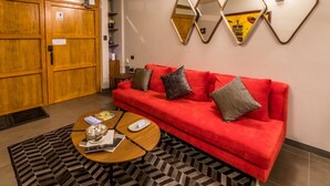 A red sofa with multiple cushions, a wooden coffee table with a magazine and a bowl, and a patterned rug. - Casa Olié (Oaxaca)