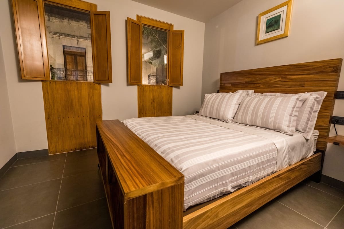 A bedroom with a wooden bed, a bench, and two wooden-framed windows.