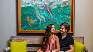 A couple sitting on a wooden bench with a colorful abstract painting above them. - Casa Olié (Oaxaca)