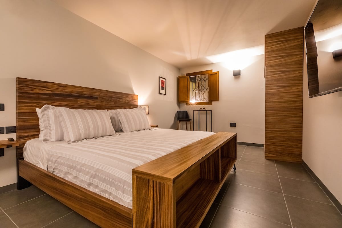 A modern bedroom with a wooden headboard, a large bed with white bedding, a bedside table, and a nightstand.
