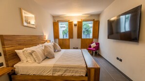 A modern bedroom with a wooden bed, a flat-screen TV, and a view of the outside through windows. - Casa Olié (Oaxaca)
