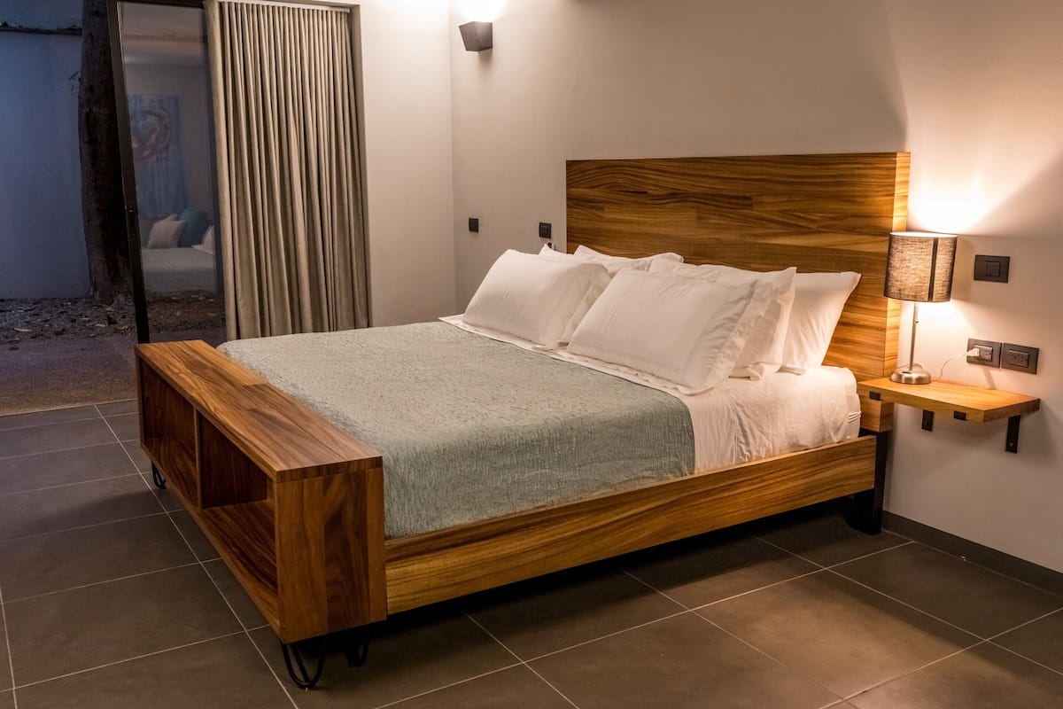 A modern bedroom with a wooden bed, a bedside table with a lamp, and a view of the outside.