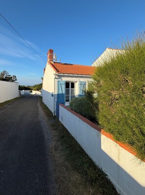 A white house with a red-tiled roof, a blue door, and a small garden.