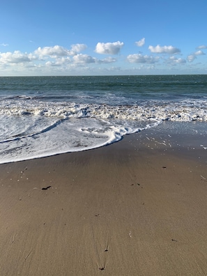 A beach with waves reaching the shore, a clear sky, and a calm sea.