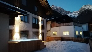 A snow-covered courtyard with a wooden deck, a heated outdoor seating area, and a mountain backdrop. - Luxury Apart. mit 2 Schlafzimmern Terrasse (Antholz Mittertal)