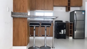 A modern kitchen with wooden cabinets, a stainless steel refrigerator, and two bar stools.
