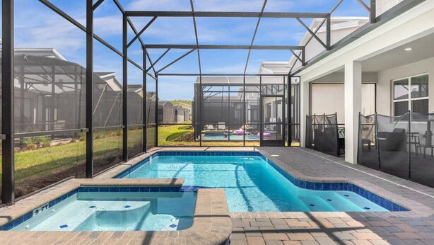 A rectangular swimming pool with a hot tub, surrounded by a covered patio area with a view of a residential neighborhood. - Dream Vacation Getaway next to Disney with Private Pool --10BD/5BA (Kissimmee)