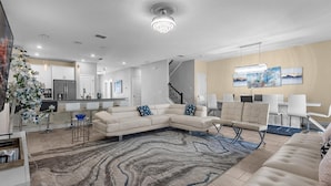 A modern living room with a sectional sofa, a dining area with chairs, a kitchen in the background, and a staircase. - Dream Vacation Getaway next to Disney with Private Pool --10BD/5BA (Kissimmee)