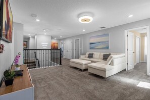 Relax in a spacious living area with a comfortable sofa and ottoman, surrounded by a large abstract painting and natural light.