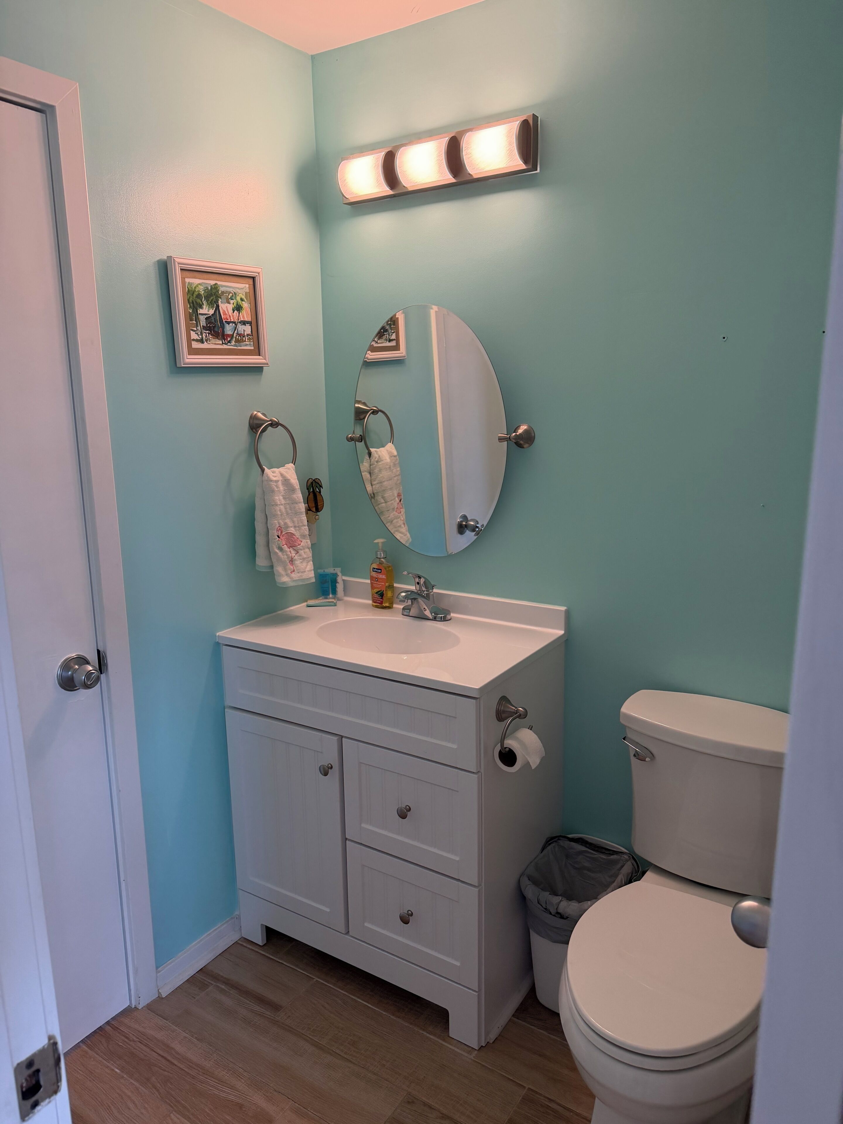 A bathroom with a sink, mirror, toilet, and a trash bin.