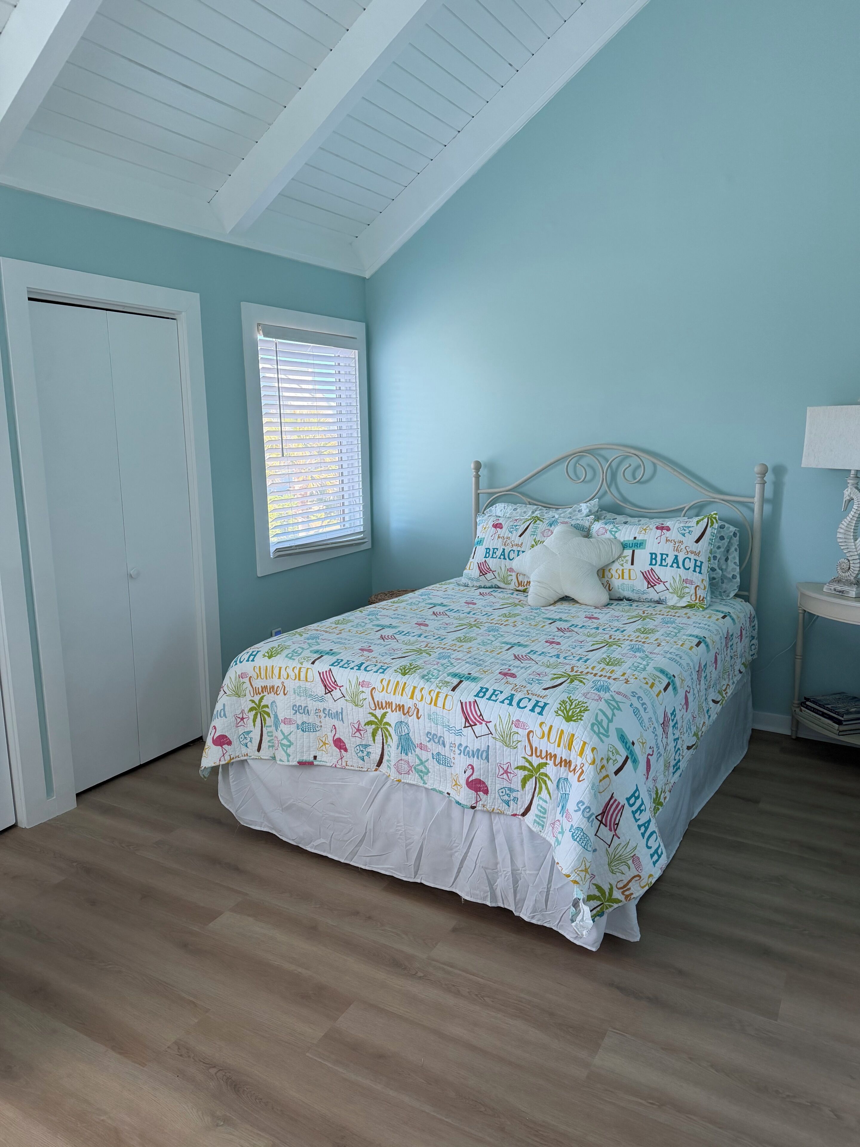 Une chambre à coucher avec un lit, une fenêtre avec des stores, une table de chevet et une porte.