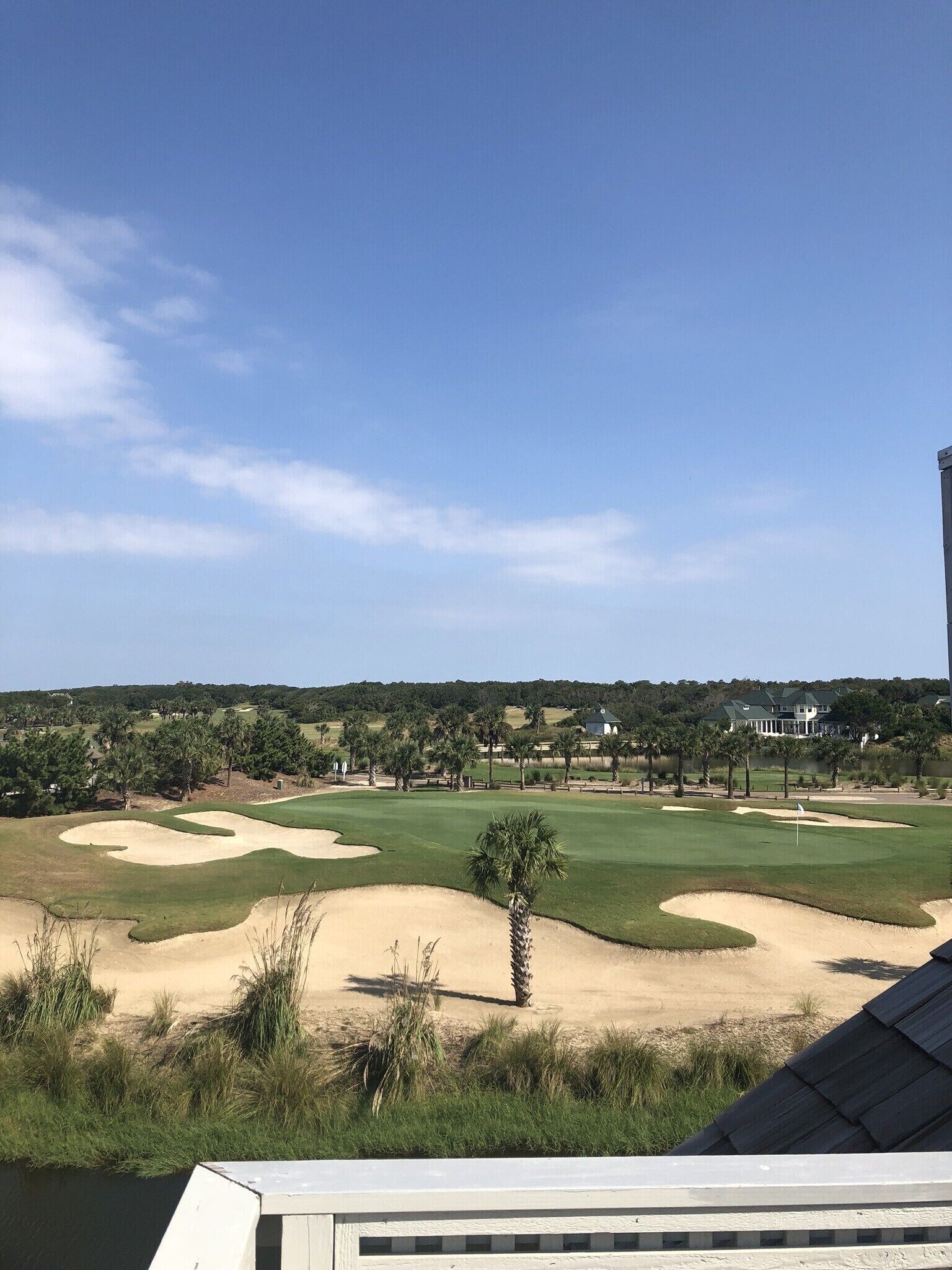 Een golfbaan met zandbunkers, palmbomen en een clubhuis op de achtergrond.