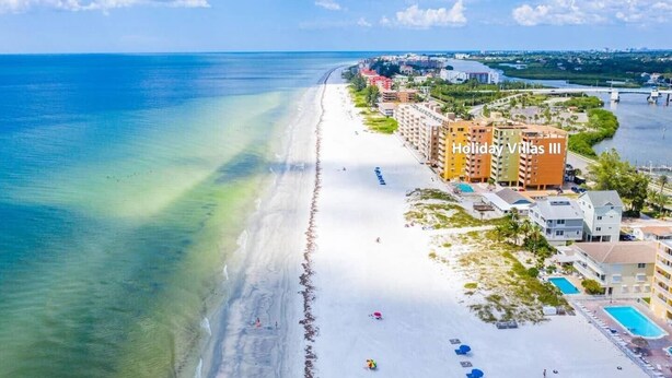Un hotel frente a la playa con varias edificaciones, una playa de arena y una vista despejada del océano.