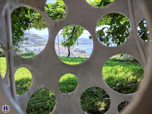 A circular window with a view of a tree and a distant cityscape. - Villa Neptune at the beginning of the Amalfi Coast CIN No. IT065157B4VGM390GL. (Raito)