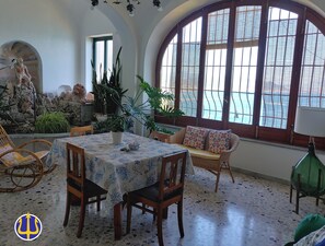 A dining area with a table set for four, surrounded by wooden chairs. There are potted plants and a statue on the wall. - Villa Neptune at the beginning of the Amalfi Coast CIN No. IT065157B4VGM390GL. (Raito)