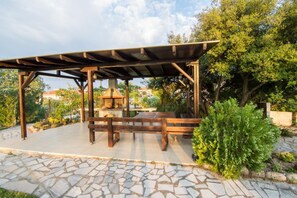 Un área de estar al aire libre cubierta, con suelo de losas de piedra y un banco de madera.