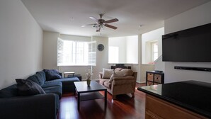A living room with a sofa, armchair, coffee table, and a flat-screen TV mounted on the wall. - Marina Bay Saddle (Richmond)