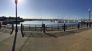 A waterfront promenade with a metal railing, street lamps, and a clear view of boats in the background. - Marina Bay Saddle (Richmond)