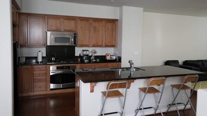 A modern kitchen with wooden cabinets, stainless steel appliances, and a bar area with bar stools. - Marina Bay Saddle (Richmond)