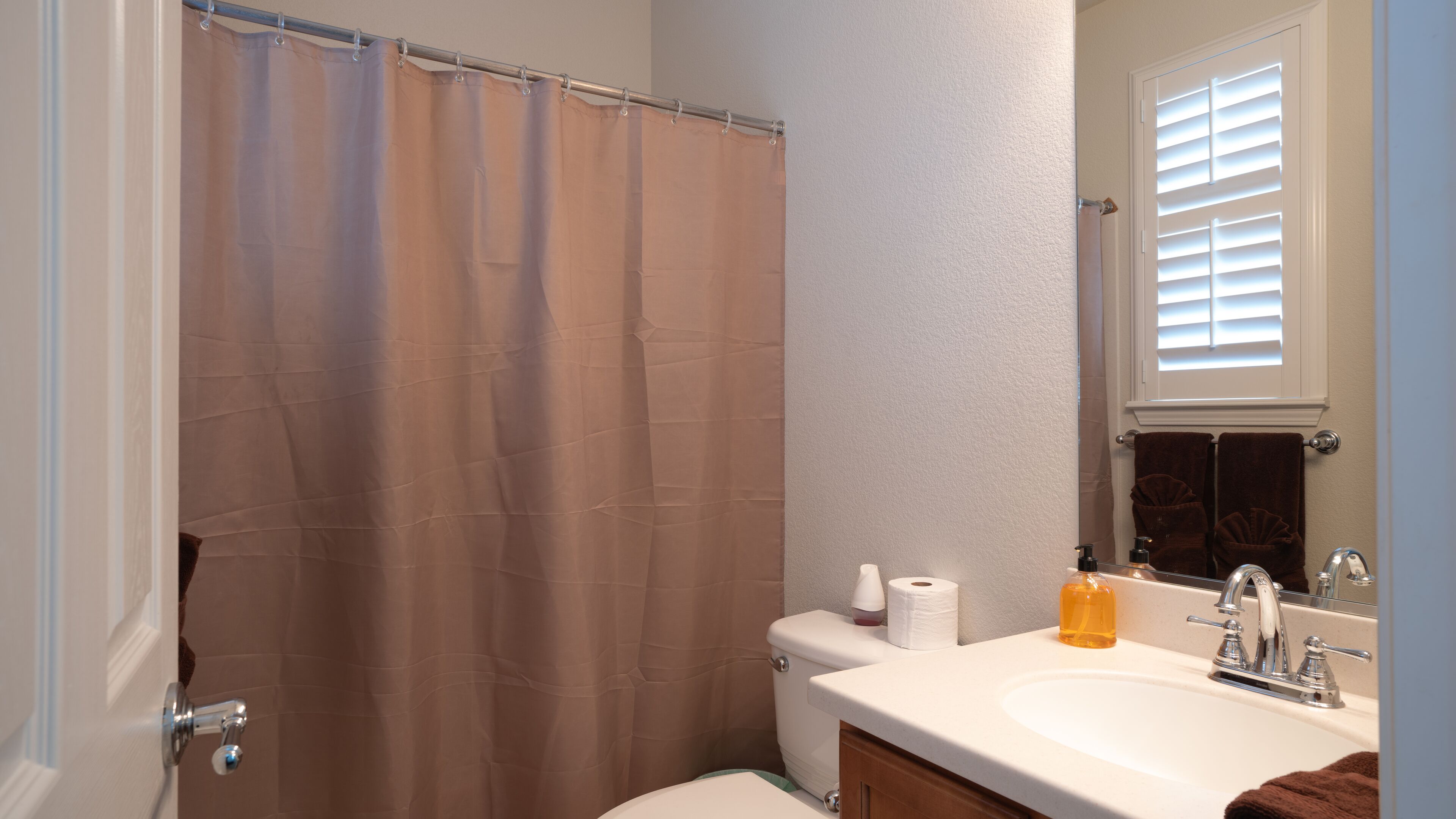 A bathroom with a shower curtain, toilet paper, a sink with soap dispenser, and a towel rack with towels.
