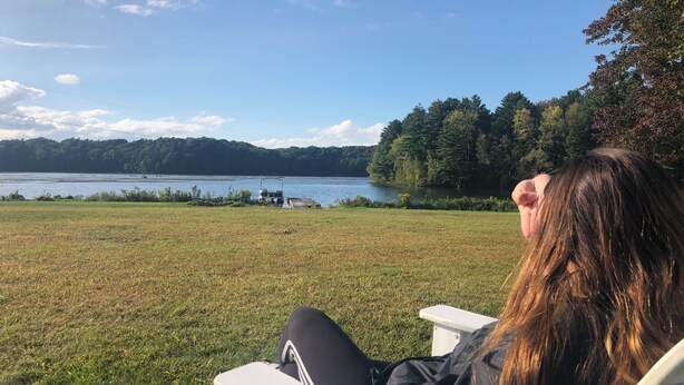 A person seated outdoors with a view of a lake and forested hills. - Majestic House on 23 acres with 5k feet of lakefront  (Fairfax)