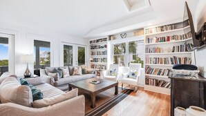 Een ruime woonkamer met een grote bank, een salontafel en een boekenplank vol boeken.