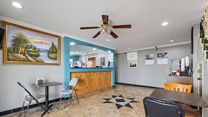 A hotel lobby with a reception desk, seating area, and a large landscape painting on the wall. - Days Inn by Wyndham Kenedy/Karnes City (Kenedy)