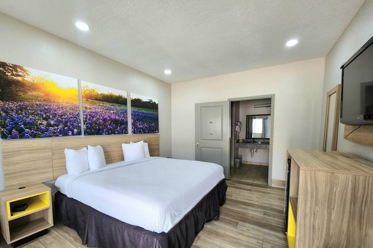 A hotel room with a large bed, a wooden nightstand, a desk, and a bathroom visible through an open door.