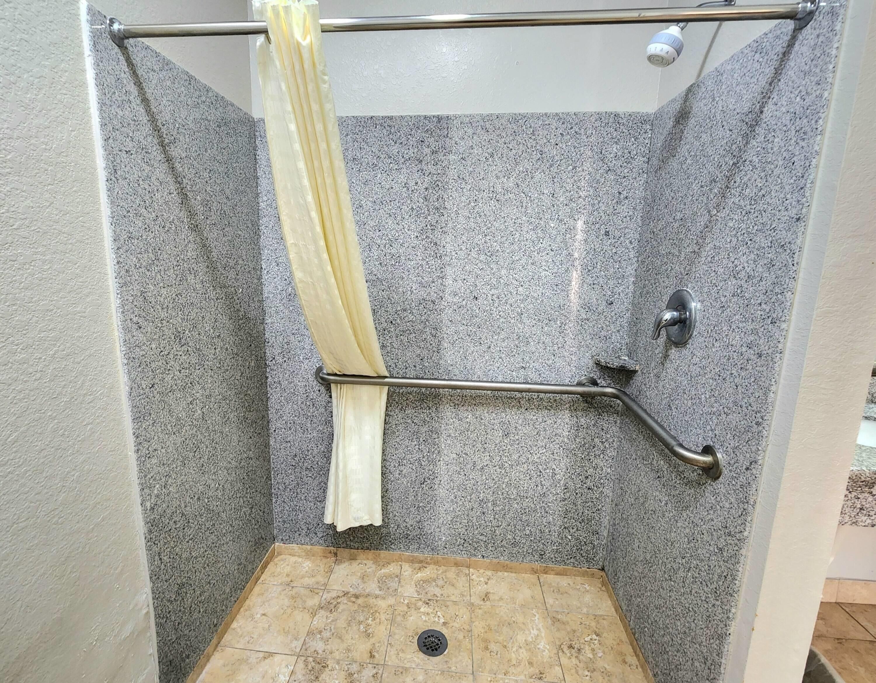 A shower with a grab bar, a shower curtain, and a handheld showerhead.
