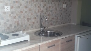 A kitchen with wooden cabinets, a stainless steel sink, a built-in stove, and a tiled backsplash. - Finikas Apartments Polichrono (Kassandra)