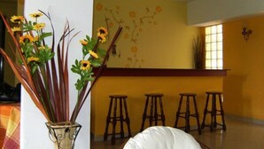 A room with a white cushioned chair, a vase with yellow flowers, and a yellow wall with a floral mural. - Finikas Apartments Polichrono (Kassandra)