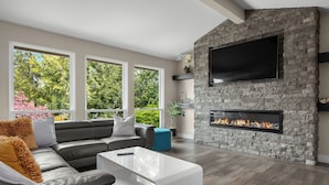 A modern living room with a stone fireplace, a large flat-screen TV, and a grey leather sofa.