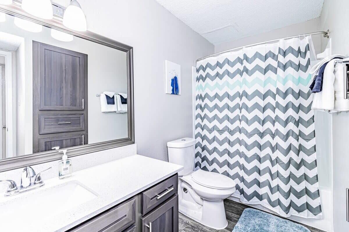 Een badkamer met een wit wastafel, een spiegel, een toilet en een douchegordijn met een zigzagpatroon.