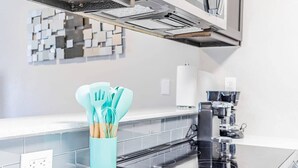 Une cuisine moderne avec une plaque de cuisson à induction noire, une machine à café et un porte-ustensiles de couleur turquoise sur le plan de travail.