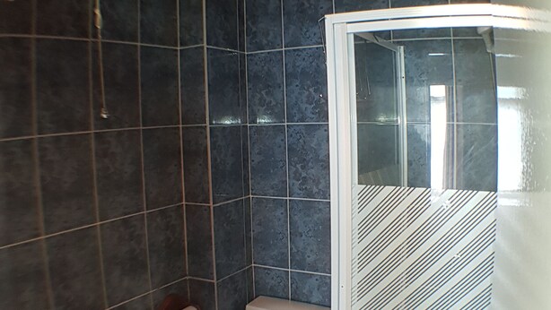 A bathroom with dark tiled walls, a toilet, a sink, and a shower enclosure. - Glen Villa Flat 2 - 6 Berth (Great Yarmouth)