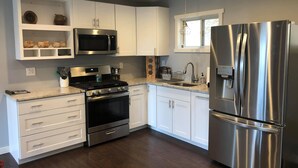 Una cocina moderna con armarios blancos, electrodomésticos de acero inoxidable y un ventanal sobre el fregadero.