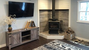 Una sala de estar con chimenea, televisor montado en la pared y mueble bajo de madera.