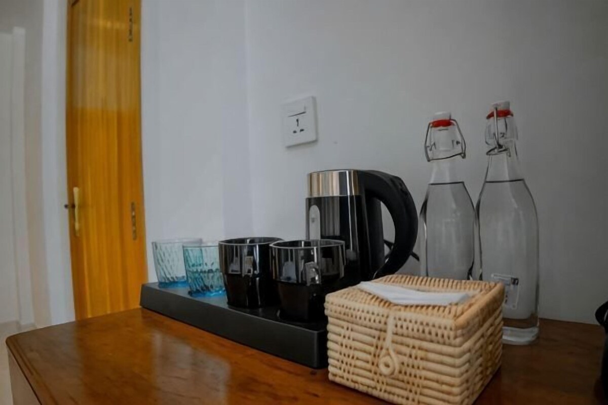 A wooden table with a coffee maker, glass bottles, and a wicker basket.