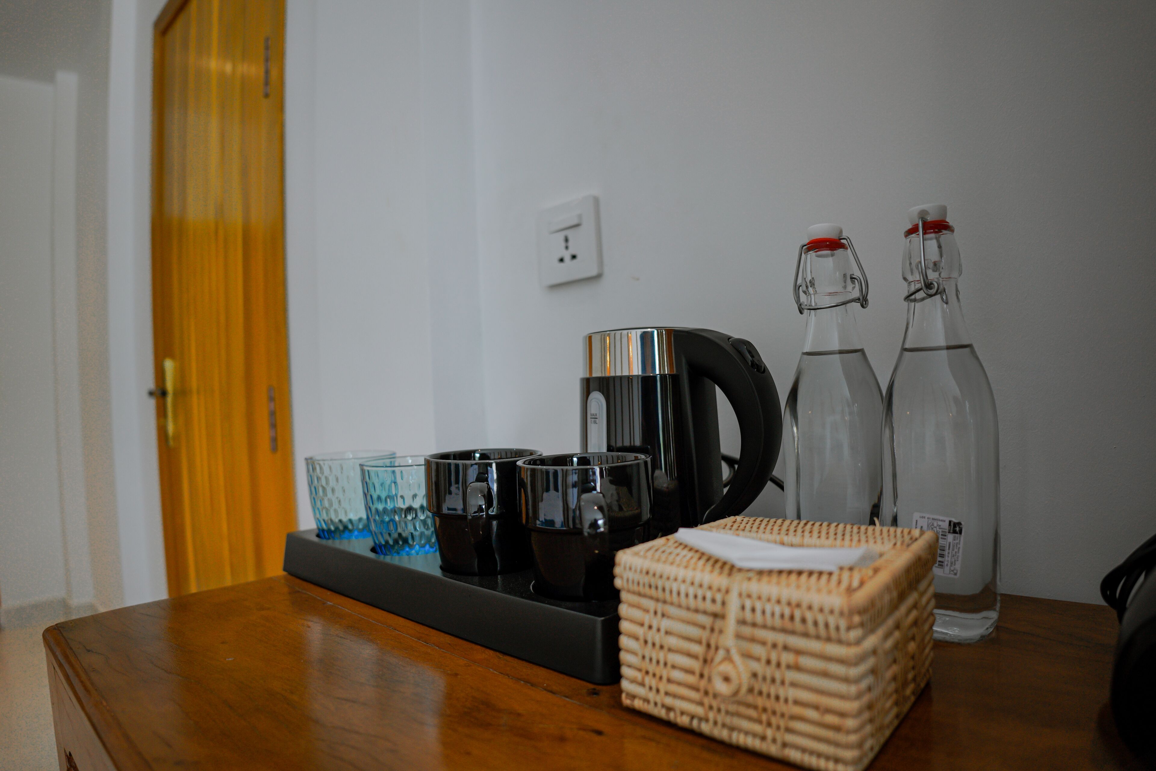 A wooden table with a coffee maker, two bottles, and a basket of bread.