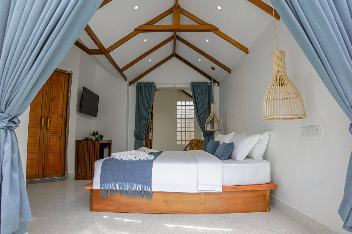 A bedroom with a wooden bed, blue curtains, a television, and a hanging light fixture.
