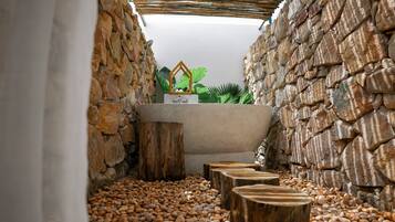 Un espace de détente aux murs de pierre, avec un banc en bois et une petite fontaine.